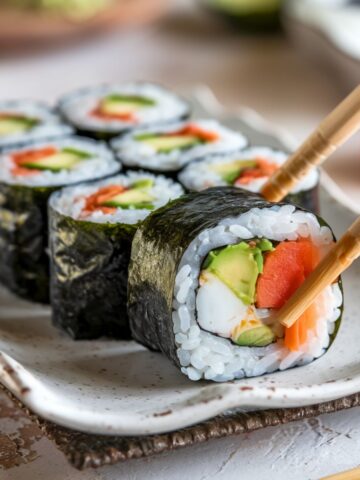 Close-up of sushi rolls with avocado, salmon, and crab, picked up with chopsticks in sushi roll recipe