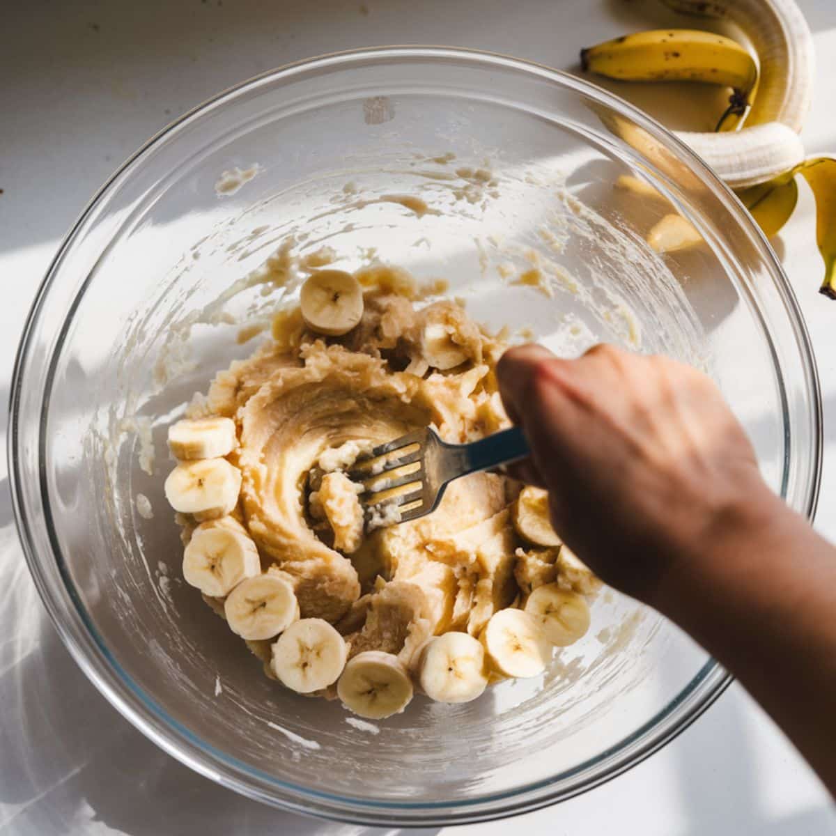 Mashing bananas with a fork in a glass bowl for a banana bread recipe.