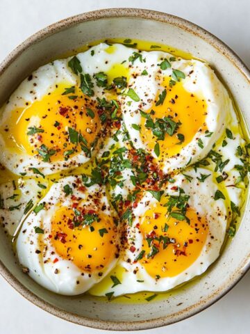 Turkish eggs recipe (Çılbır) served in a bowl with chili butter and herbs