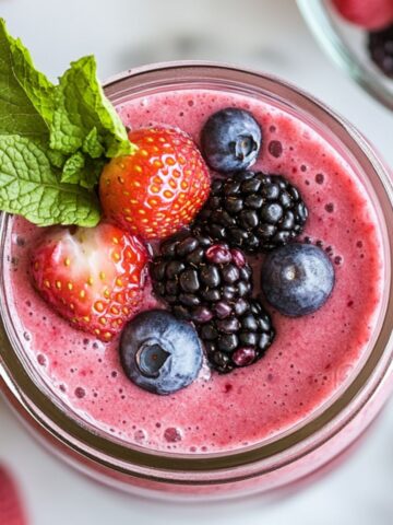 Serving a fresh berry smoothie recipe in a glass jar with berries and mint garnish on a clean white marble kitchen counter.