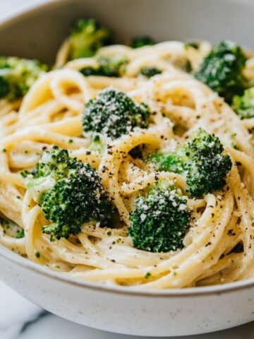 A bowl of creamy broccoli pasta recipe with broccoli and penne on a white marble kitchen counter, showcasing a homemade, cozy vibe.
