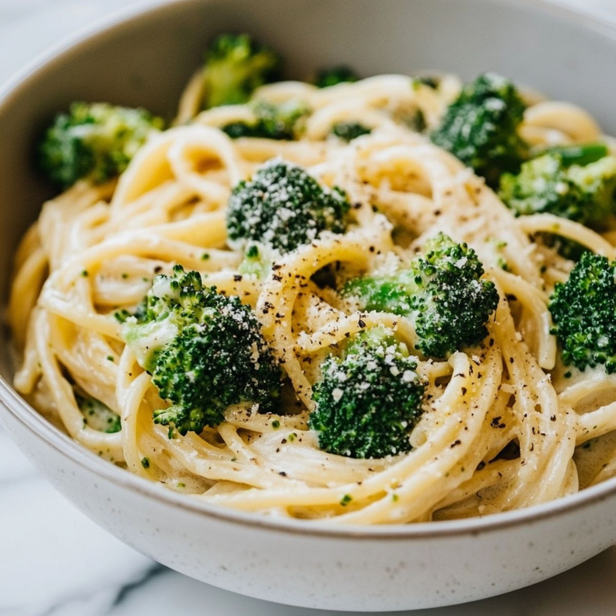 A bowl of creamy broccoli pasta recipe with broccoli and penne on a white marble kitchen counter, showcasing a homemade, cozy vibe.