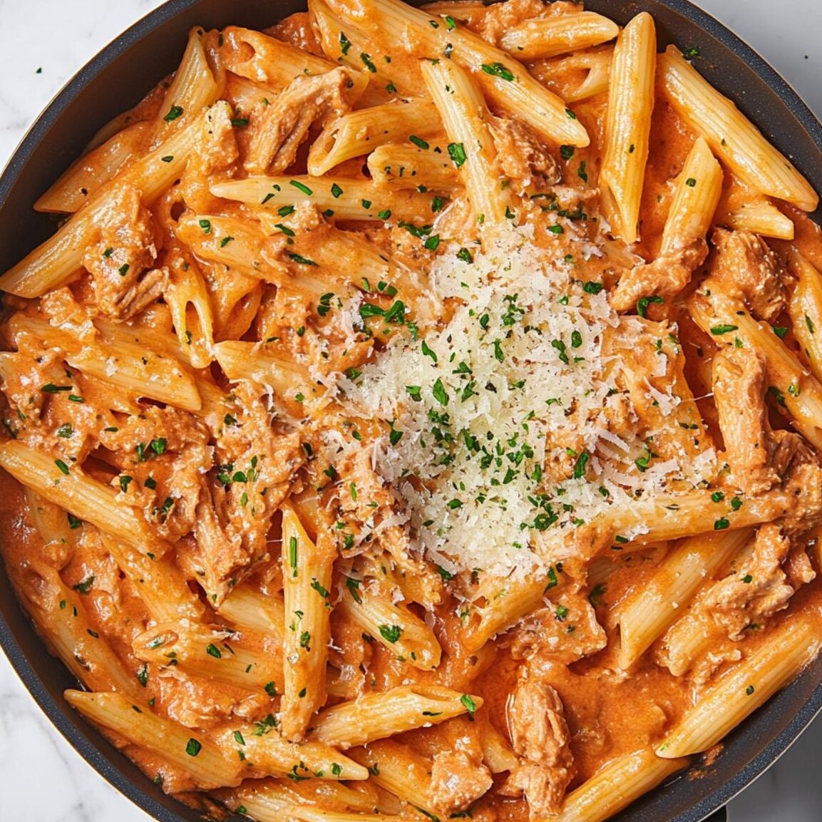 Creamy tuna pasta with parsley being tossed in a skillet