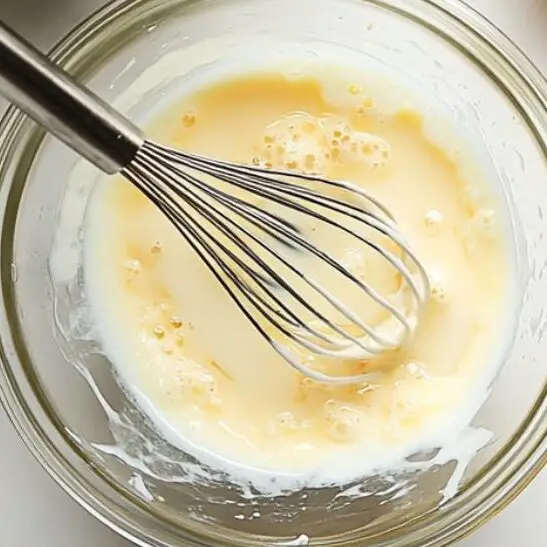 Pouring hot milk into egg mixture in glass bowl