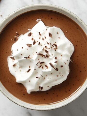 Homemade chocolate pudding topped with whipped cream on a white marble kitchen counter.