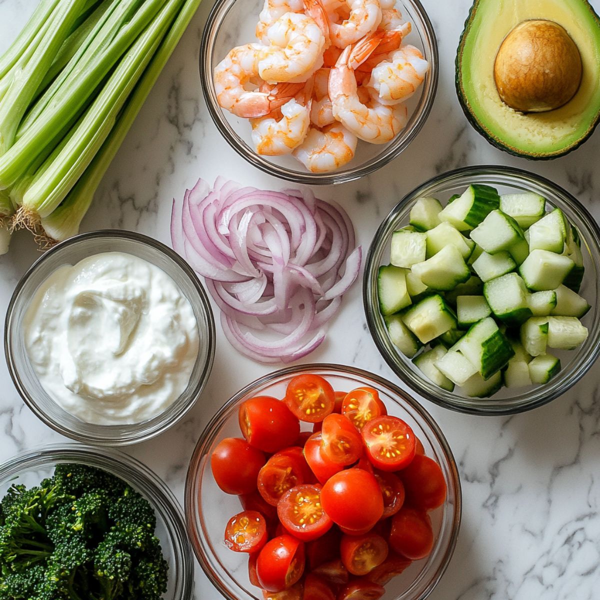 Fresh ingredients for shrimp salad including shrimp, vegetables, and avocado on a wooden cutting board.
