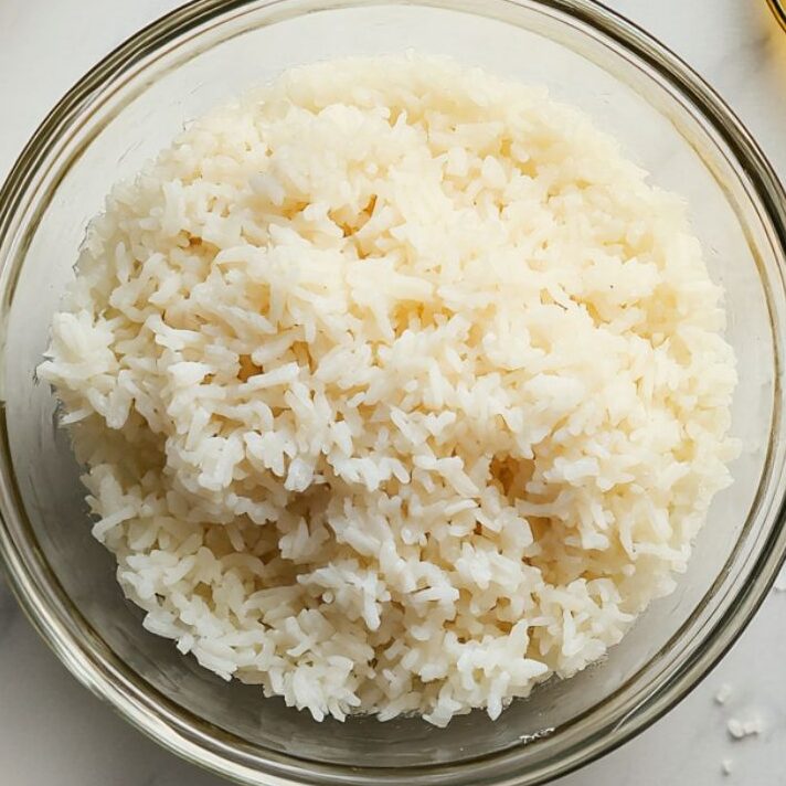 Preparing rice in a glass bowl for tuna poke bowl on white marble kitchen counter