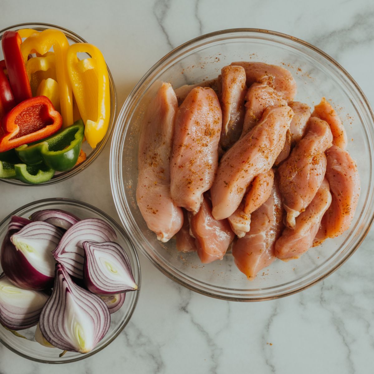 Chicken fajita casserole recipe ingredients in glass bowls on a white marble counter