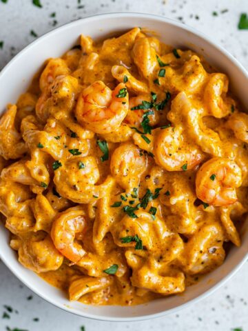 Creamy cajun shrimp pasta served in a white bowl with herbs on top.