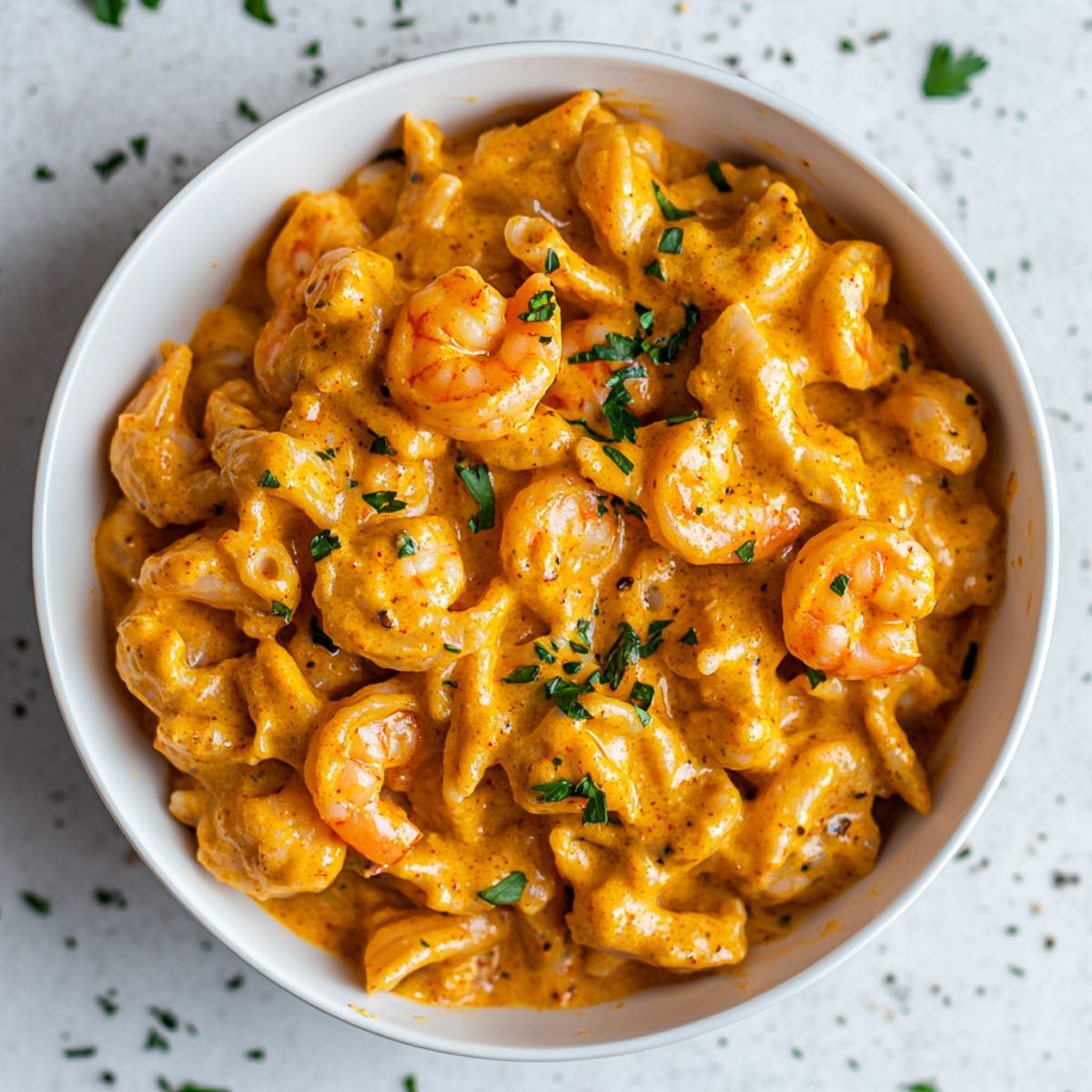 Creamy cajun shrimp pasta served in a white bowl with herbs on top.