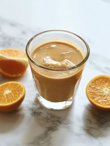 Homemade orange smoothie recipe in a clear glass on a white marble counter