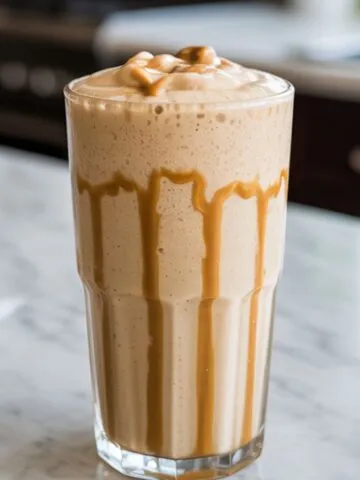 Glass of peanut butter shake recipe with a creamy swirl, served on white marble kitchen counter