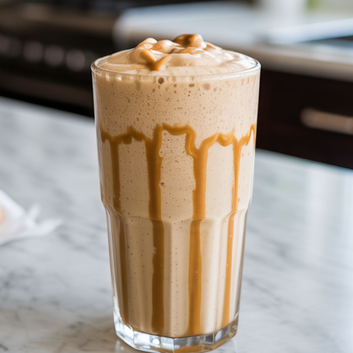 Glass of peanut butter shake recipe with a creamy swirl, served on white marble kitchen counter