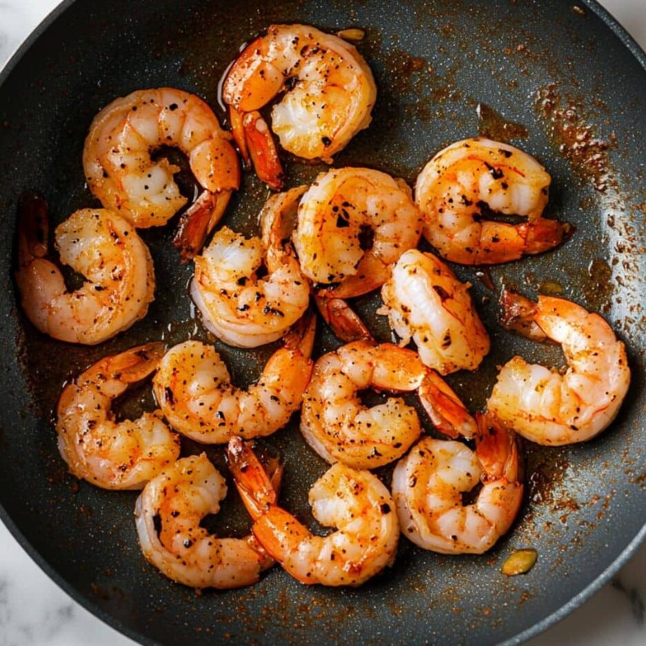 Shrimp cooking in a skillet on a clean stovetop.