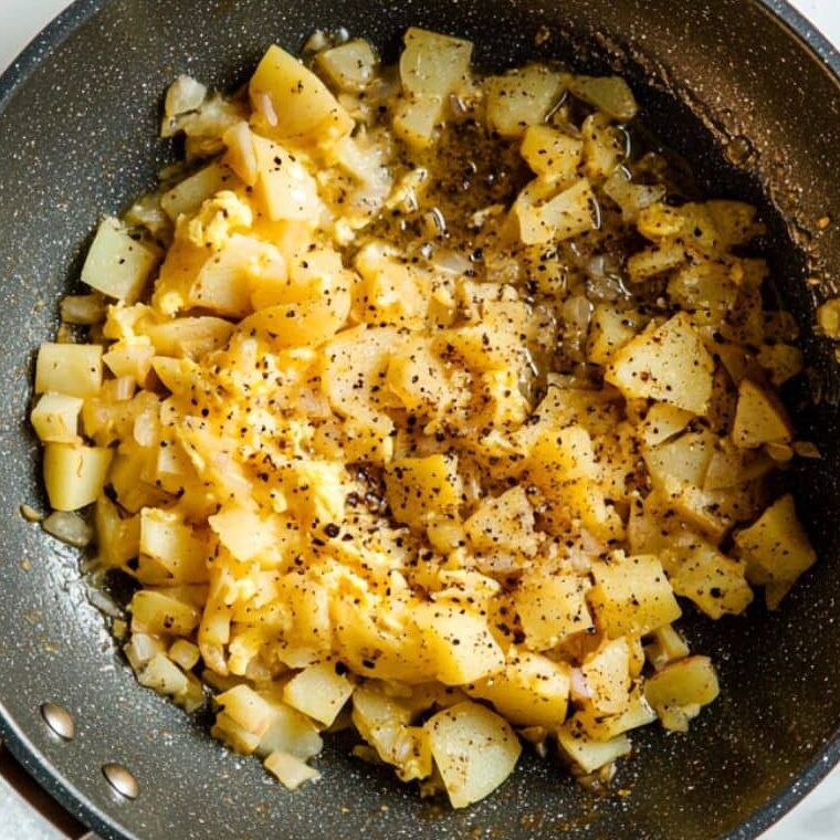 Egg and potato mixture cooking in a non-stick pan for Tortilla Española.

