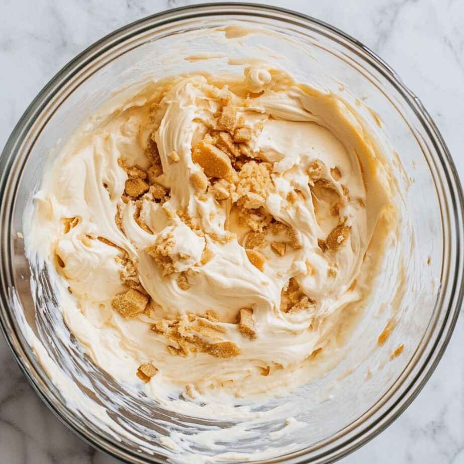 Creamy Biscoff cheesecake filling in a glass bowl ready to be poured into crust.
