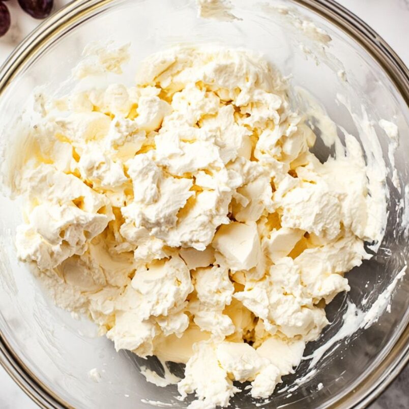 Cream cheese filling being mixed in a glass bowl on white marble counter