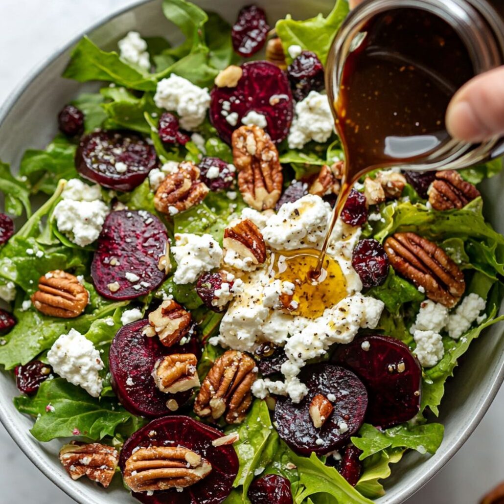 Glass bowl with partially assembled goat cheese salad on a white marble surface.