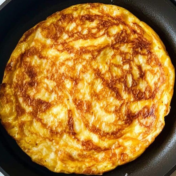 Tortilla Española cooking on second side after flipping in a skillet.