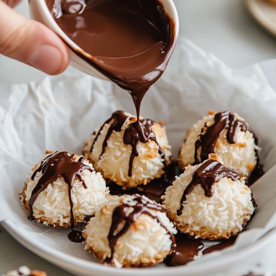 Coconut macaroons being dipped in chocolate on a white marble kitchen surface