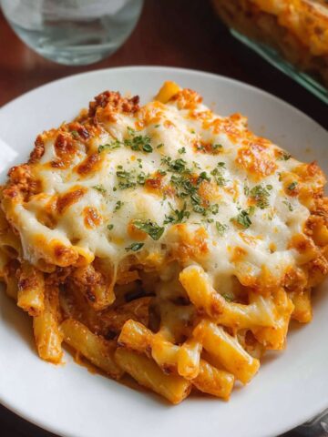 Cheesy baked ziti recipe with golden melted cheese in a glass baking dish on white marble counter