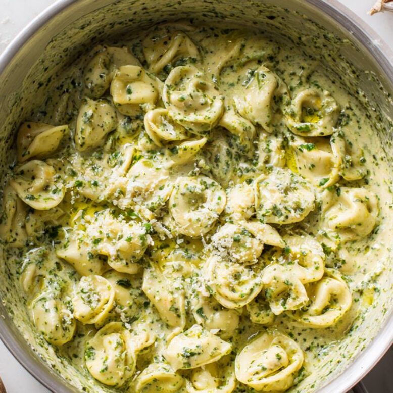 Mixing tortellini with creamy pesto and garlic in a bowl