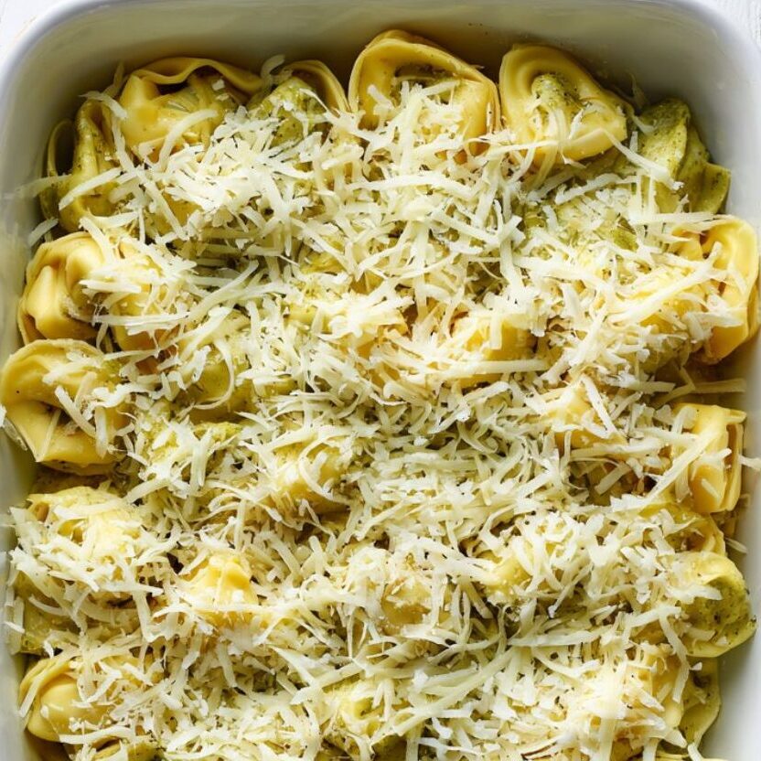 Topping pesto tortellini with cheese before baking