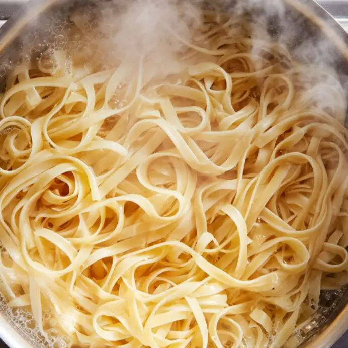 Fettuccine pasta boiling in salted water on a white kitchen stovetop

