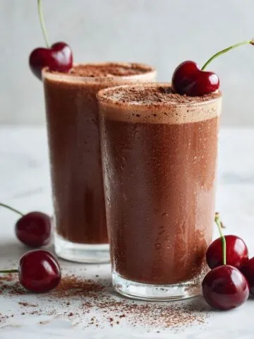 Chocolate cherry smoothie recipe in glass cups with cherries on top on white marble.