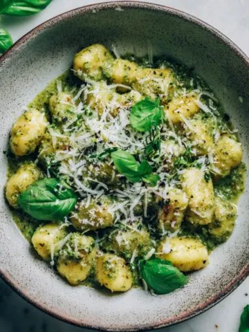 Overhead bowl of creamy pesto gnocchi recipe with basil and Parmesan on a white marble counter