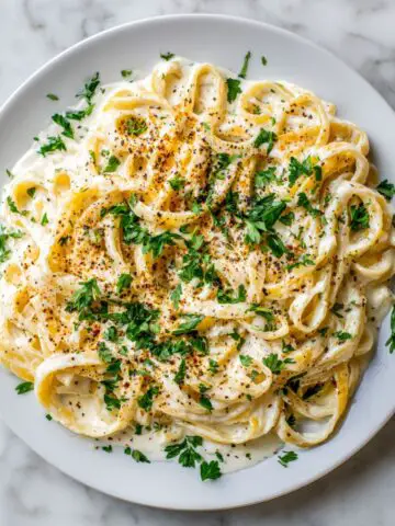 Creamy homemade Fettuccine Alfredo Recipe served on a white plate on a marble kitchen counter