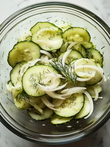 Fresh homemade cucumber salad recipe with onions and dill in a glass bowl on white marble