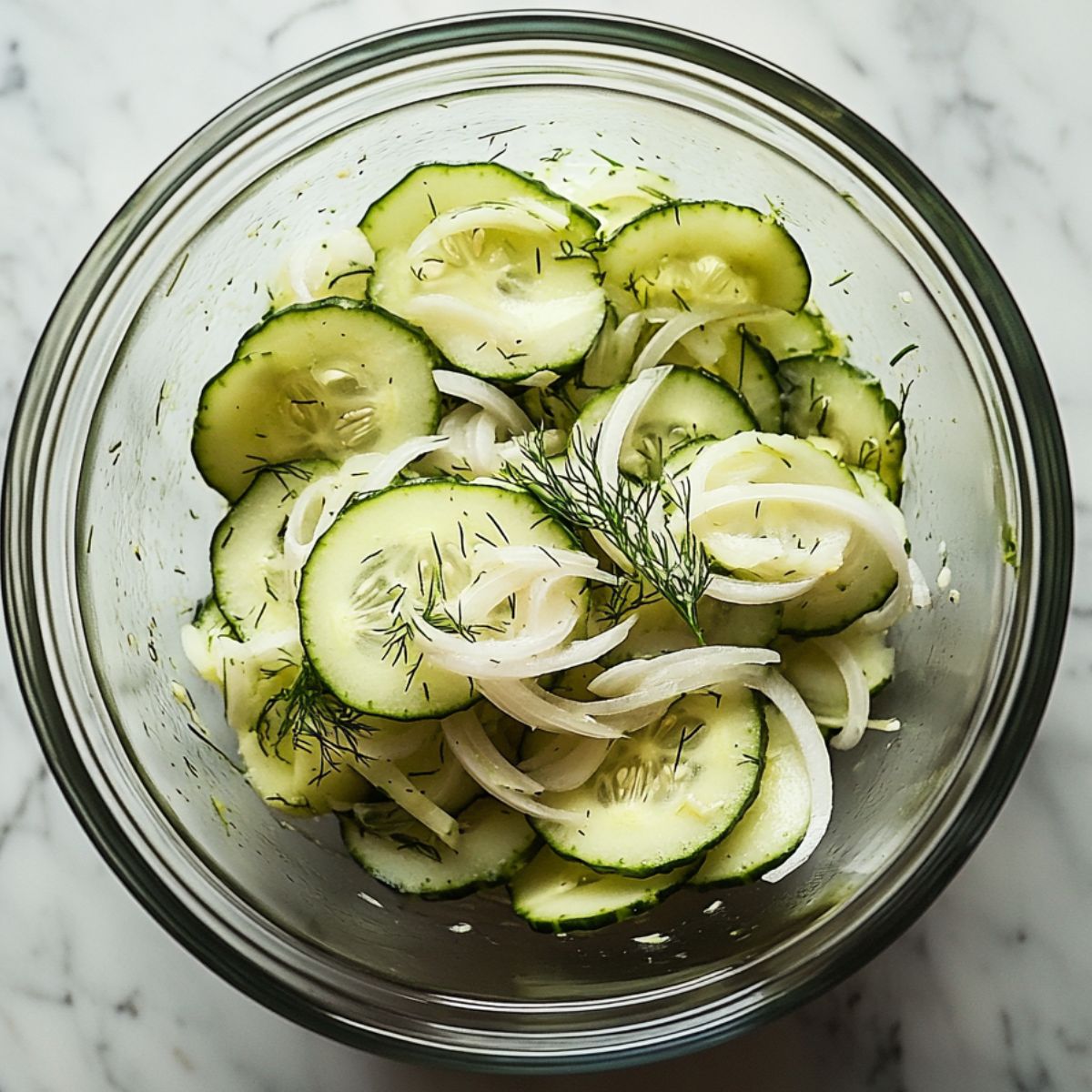Fresh homemade cucumber salad recipe  with onions and dill in a glass bowl on white marble