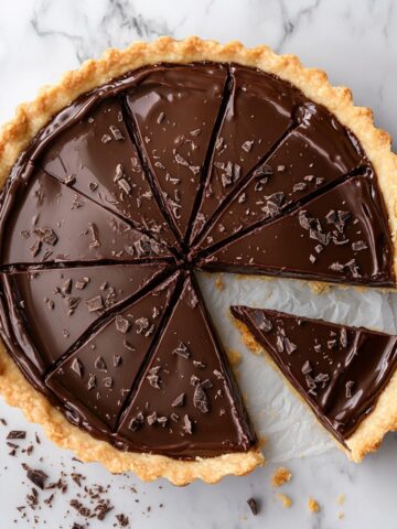 Homemade chocolate tart recipe with shiny ganache sliced on a white marble surface