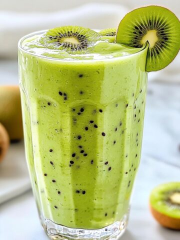 Kiwi smoothie recipe in a glass with chopped kiwi on white counter
