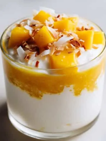 Mango coconut pudding recipe layered in glass cup with fresh mango and coconut topping.