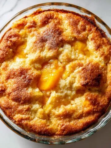 Baked peach cobbler pudding recipe in white ceramic dish on white marble counter