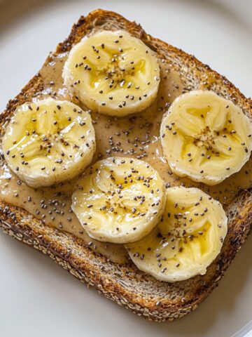 Overhead view of two almond butter banana toast recipe slices with banana, honey, and chia on a white marble kitchen counter.