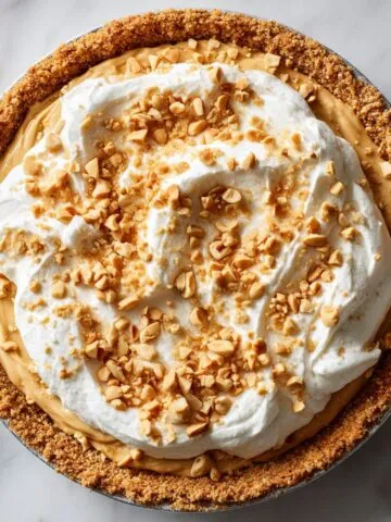 Whole peanut butter pie recipe with whipped cream and peanut topping on a white marble counter
