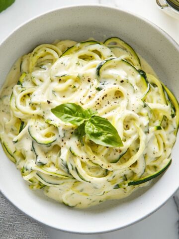 Creamy zucchini noodle alfredo recipe served in a white bowl on a marble kitchen counter
