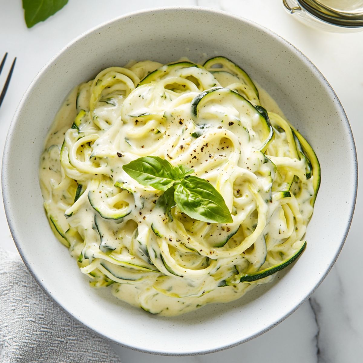 Creamy zucchini noodle alfredo recipe  served in a white bowl on a marble kitchen counter