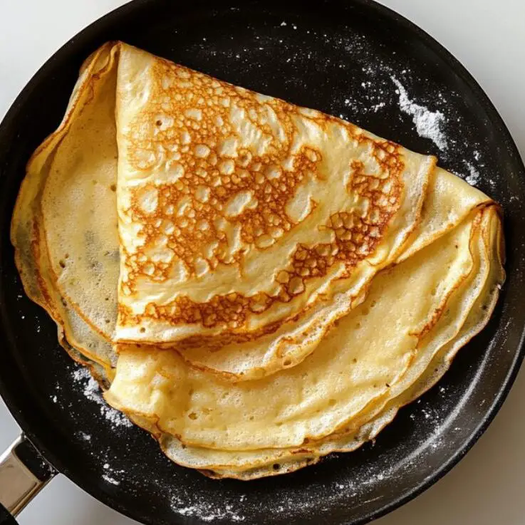 Perfectly flipped golden crepe in a pan on white marble counter.