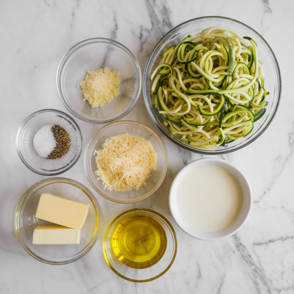 Ingredients for zucchini noodle alfredo recipe laid out on a white marble kitchen counter