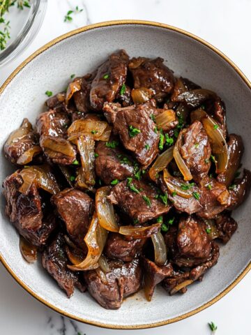 Classic liver and onions recipe in a cast-iron skillet with golden caramelized onions on a white marble countertop