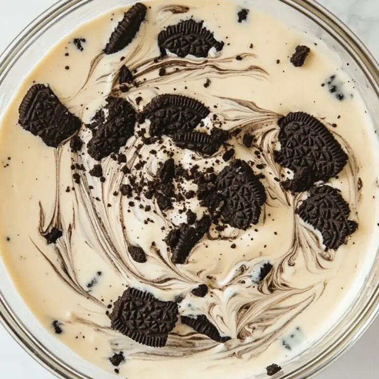 Oreo pudding mixture with visible cookie pieces and creamy swirls in a mixing bowl.