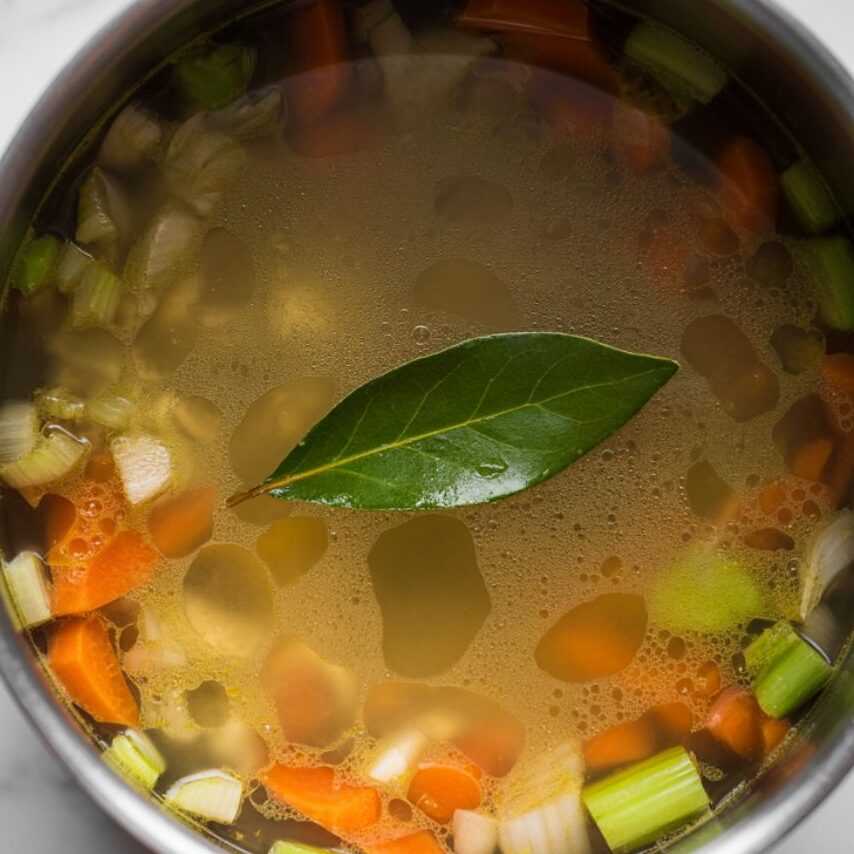 Chicken broth simmering with vegetables and bay leaf