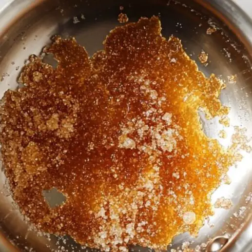 Sugar in a saucepan caramelizing to a golden color on a marble kitchen counter.

