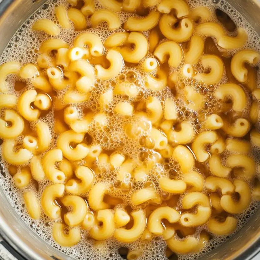 Elbow macaroni cooking in a pot on a stovtop.