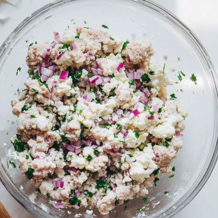 Mixing chicken, feta, and herbs in a bowl for burger patties.