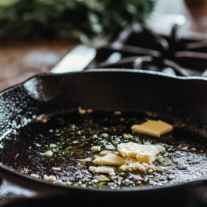 Cast iron skillet heating with garlic and butter prepped nearby